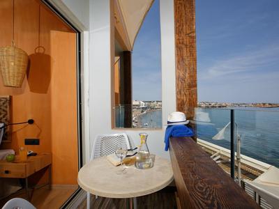 Cozy balcony with table, wine glasses, ocean view, and adjacent bedroom with wooden decor.