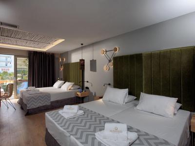 Modern hotel room with two beds, green headboards, and balcony with a view.