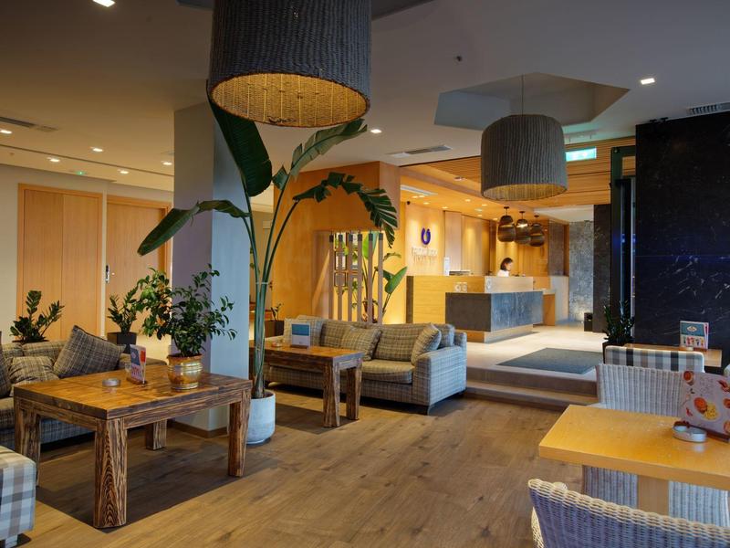 Cozy hotel lobby with wooden floors, green plants, sofas, and warmly lit seating areas.