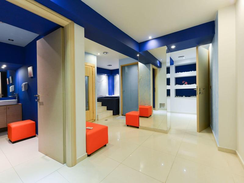 Modern hotel lobby with blue ceiling accents, mirrors, and orange seating cubes on polished floor.