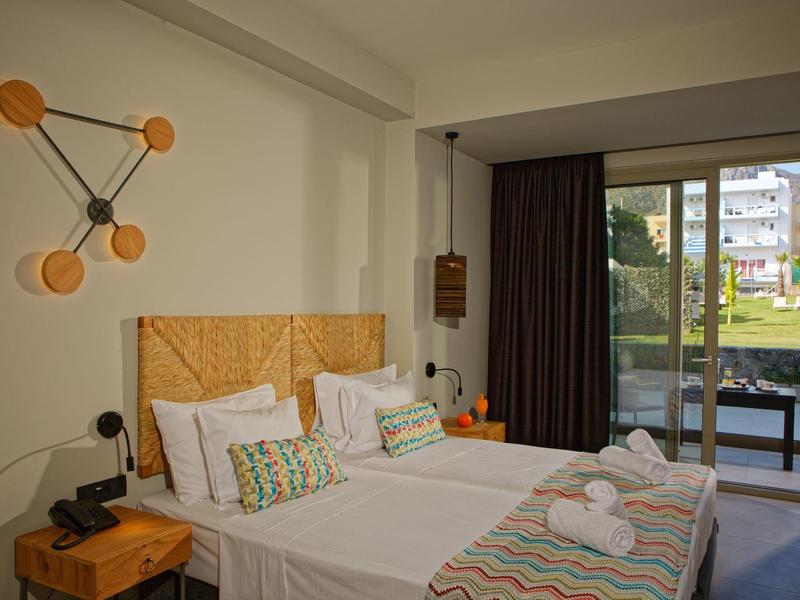 Hotel room with twin beds, modern wall lamps, and balcony overlooking garden.