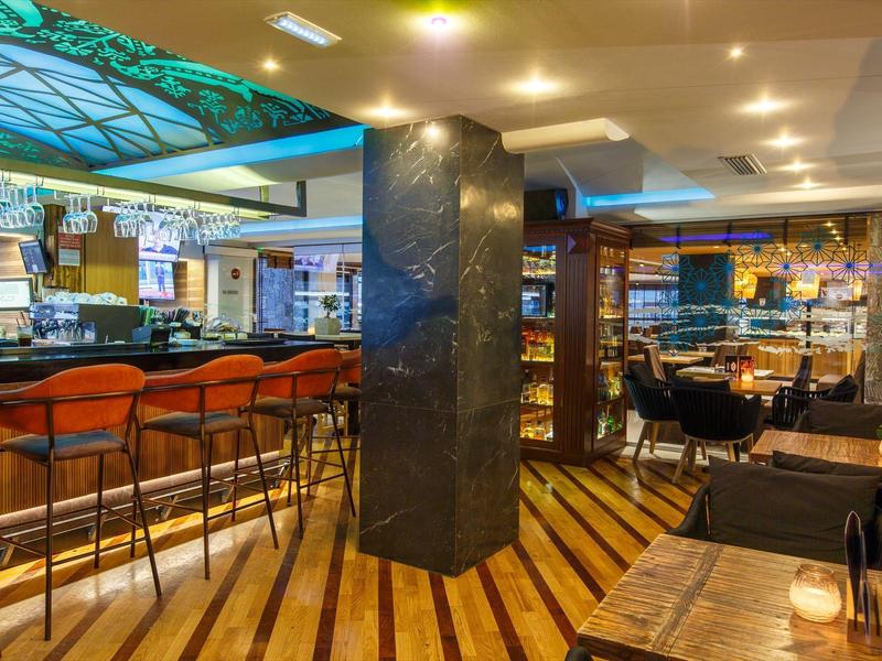 Modern bar area with orange stools, wooden floors, and ambient lighting in a hotel lounge.