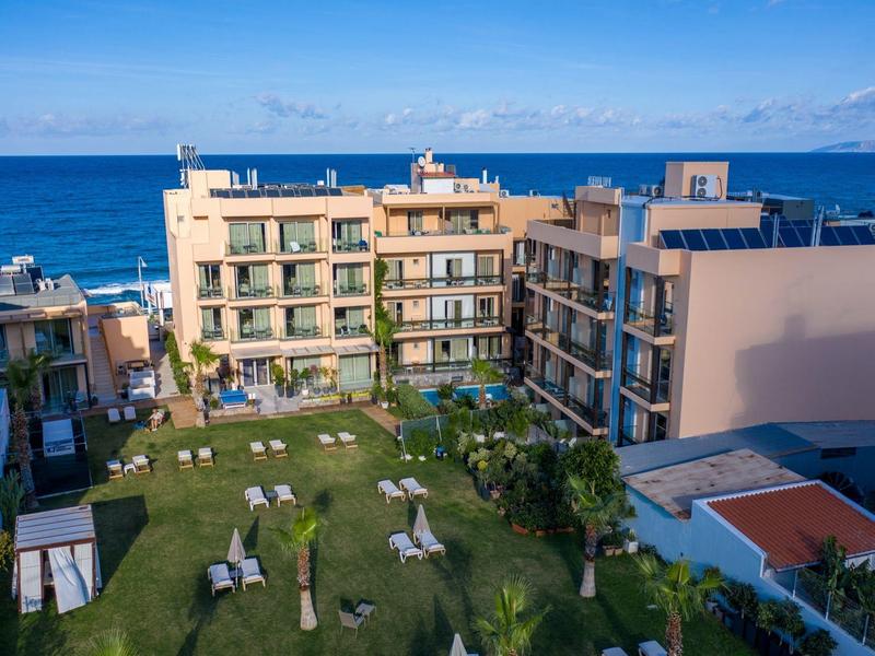 Hotel complex with green lawn facing the sea under a clear blue sky.