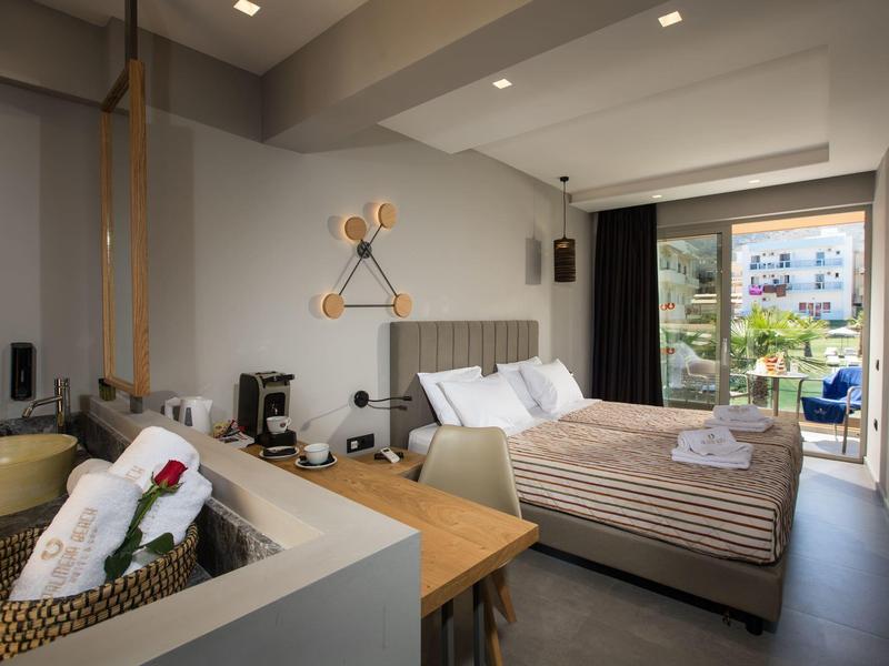 Modern hotel room with double bed, balcony, and bathroom area featuring a basket with towels.