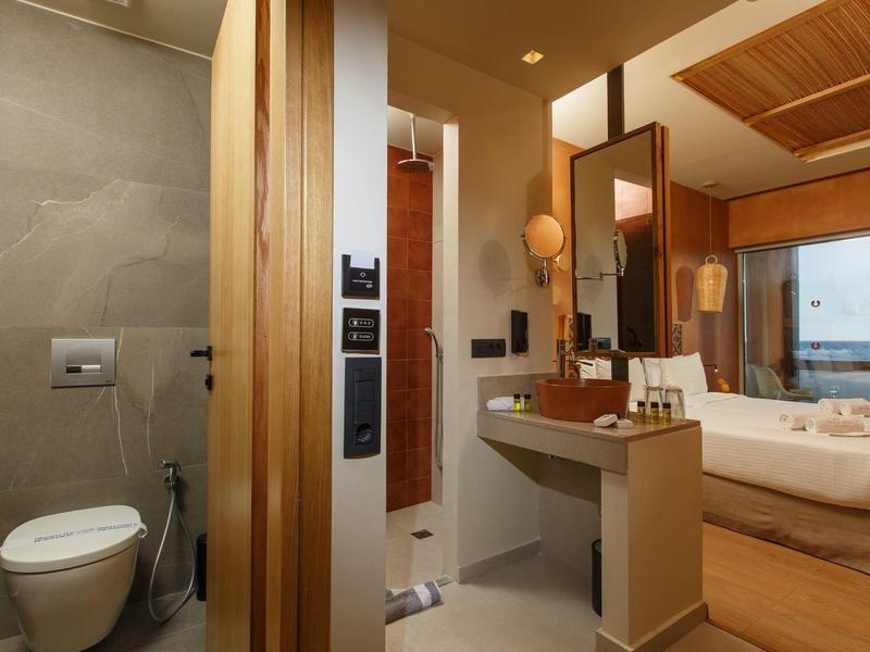 Modern hotel bathroom with toilet, vanity, and view into bedroom with sea view.