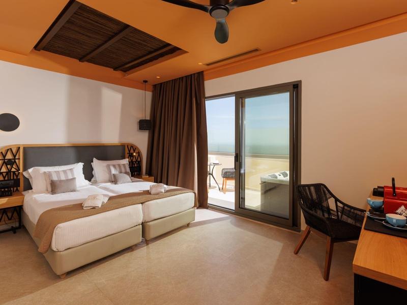 Cozy hotel room with twin beds, a desk, chair, and a balcony with sea view.