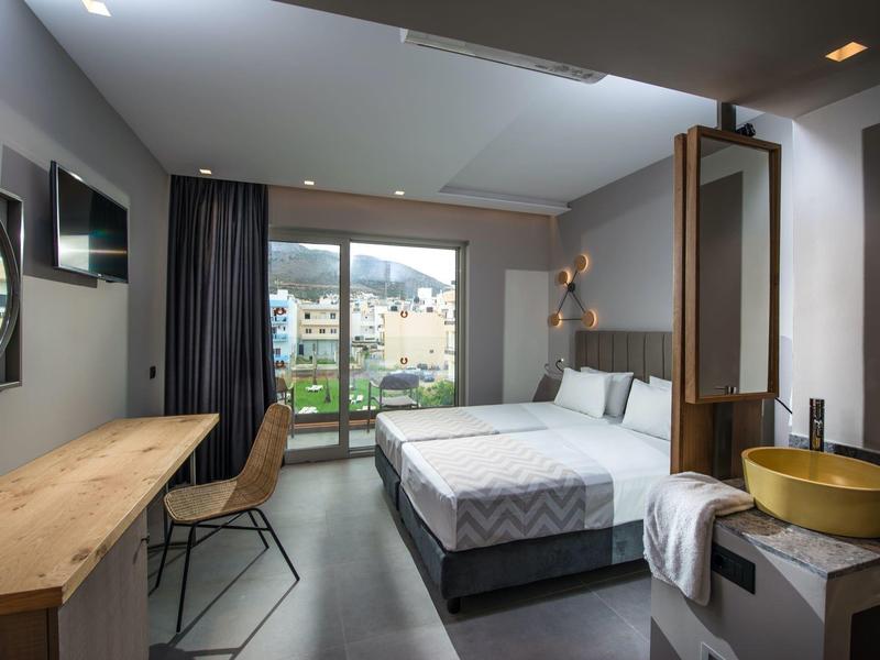 Modern hotel room with a double bed, desk, chair, balcony, and mountain view.