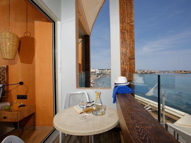 Cozy balcony with table, wine glasses, ocean view, and adjacent bedroom with wooden decor.
