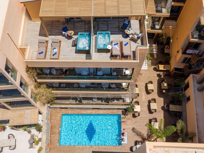Aerial view of a hotel with pool, sun loungers, and a terrace seating area.