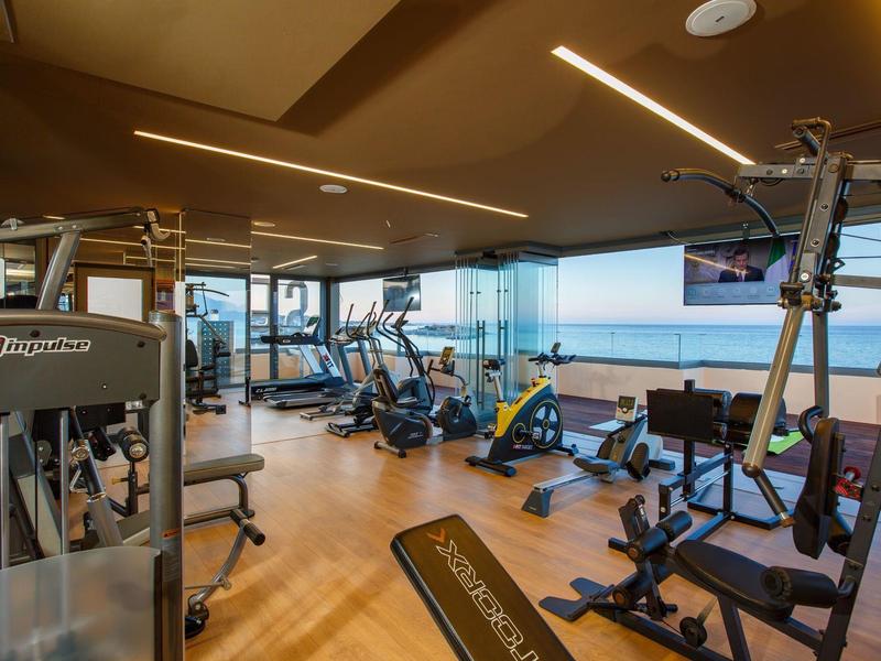 Modern gym with equipment and large window overlooking the sea.