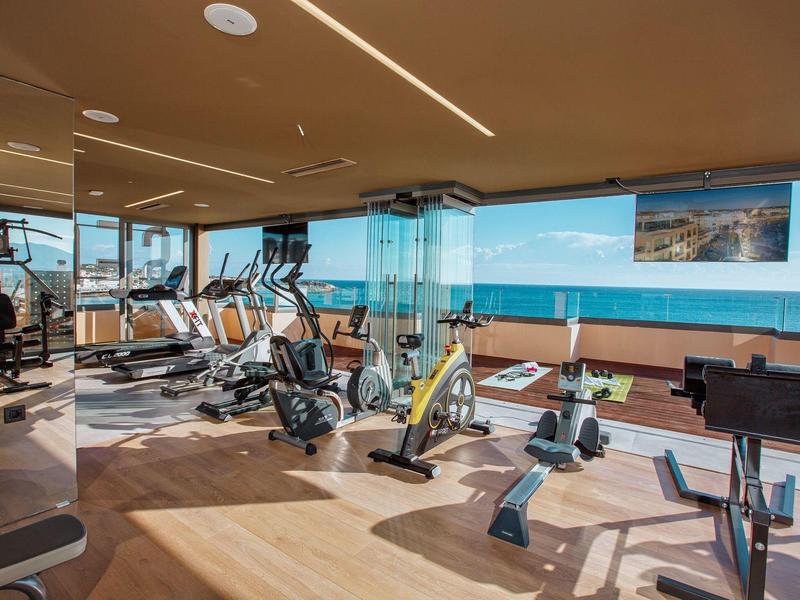 Modern gym with sea view and various exercise equipment.