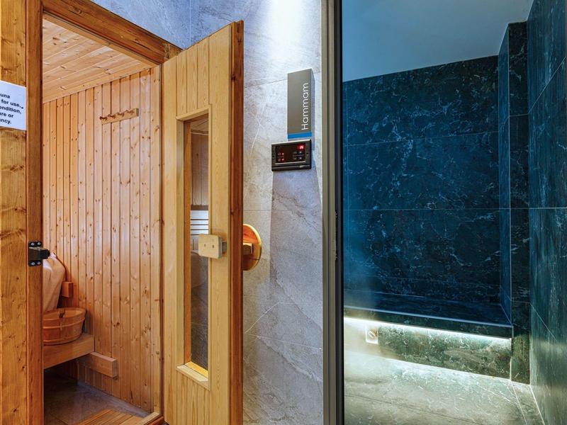 Wooden sauna next to a steam shower with modern tiles and LED lighting.
