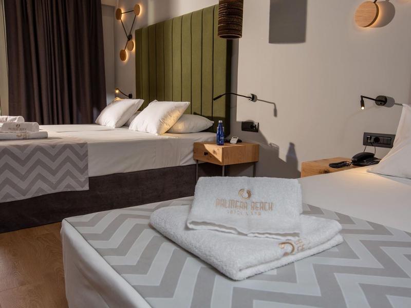 Two beds in a hotel room with gray blankets and white pillows, towels on one bed.