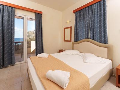 Schlichtes Hotelzimmer mit großem Bett, blauen Vorhängen und Blick auf Meer durch Glastür.