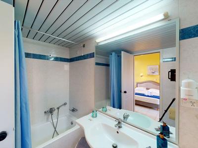 Kleines Badezimmer mit Badewanne, Spiegel, Waschbecken und blauen Akzenten an Wand und Vorhang.