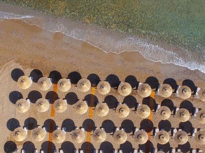 Vogelperspektive auf Strand mit abwechselnd weißen und schwarzen Sonnenschirmen am Ufer.