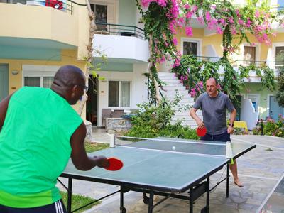 Twee mannen spelen tafeltennis buiten in een hotelbinnenplaats met bloemen.