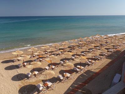 Pusta piaszczysta plaża z rzędami parasoli i leżaków nad spokojnym morzem.