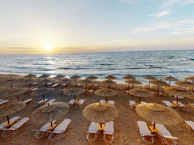 Sonnenuntergang über einem Strand mit Liegestühlen und Schirmen aus Stroh.