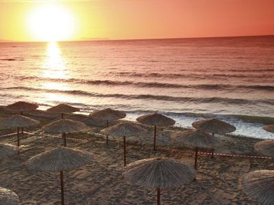 Sonnenuntergang über einem Strand mit Strohhütten und sanften Wellen im Meer