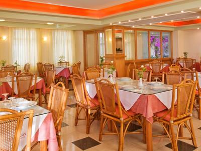 Großer heller Speisesaal mit Holzstühlen, weißen Tischdecken und warmem orangem Licht.