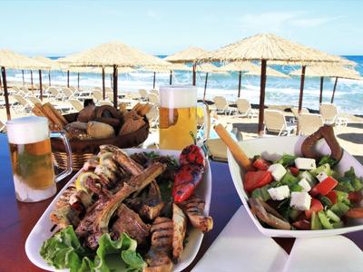 Borden met gegrild vlees, salade en bier op een tafel bij het strand met parasols.