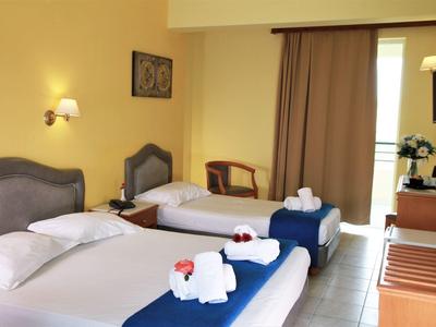 Hell eingerichtetes Hotelzimmer mit zwei Betten, weißen Handtüchern und dunklen Vorhängen.