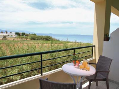 Balkon mit Tisch, Stuhl, Obst und Wein, Blick auf Felder und Meer im Hintergrund.