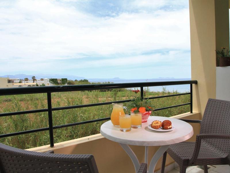 Balkon mit weißem Tisch, zwei Gläsern Saft, Keksen und zwei Stühlen, Blick auf Wiese und Himmel.