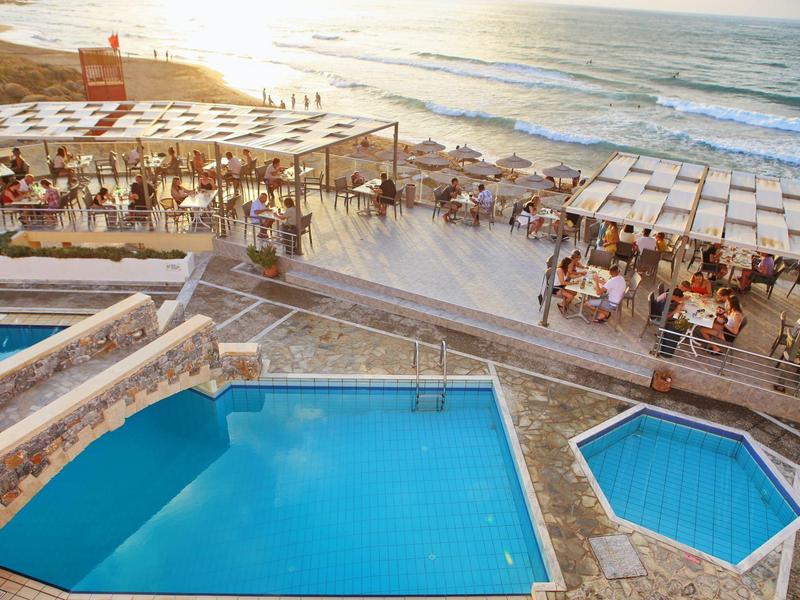 Mehrere Schwimmbecken an einer sonnigen Küste mit Menschen und Meer im Hintergrund.