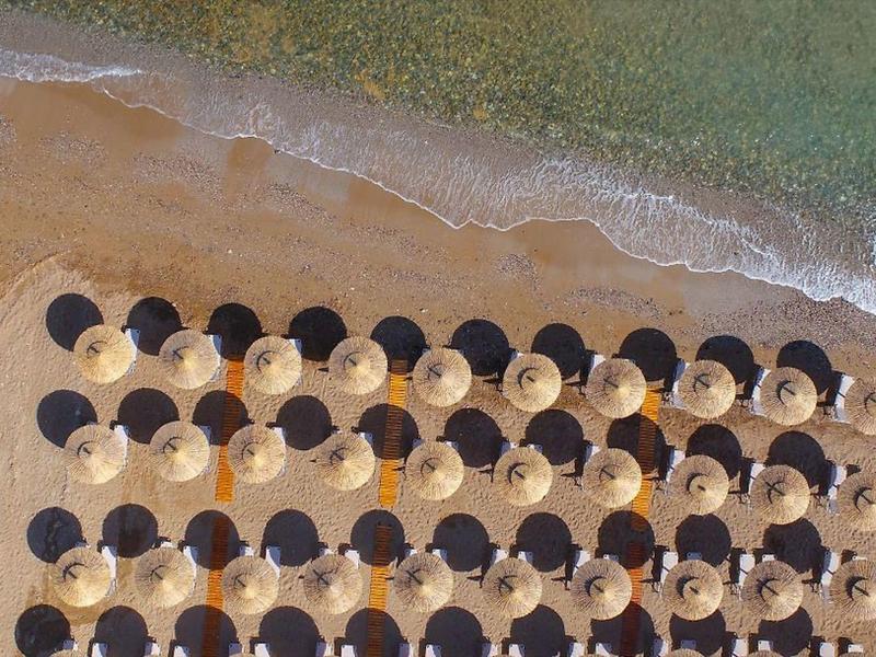Vogelperspektive auf Strand mit abwechselnd weißen und schwarzen Sonnenschirmen am Ufer.