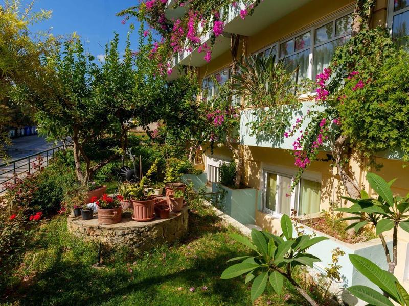 Grüner Garten mit bunten Blumen und Balkon an einem sonnigen, blauen Himmel.