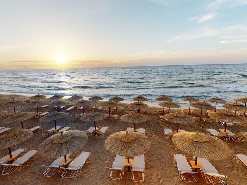 Sonnenuntergang über einem Strand mit Liegestühlen und Schirmen aus Stroh.