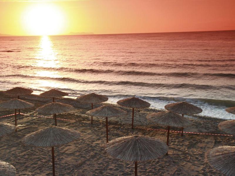 Sonnenuntergang über einem Strand mit Strohhütten und sanften Wellen im Meer