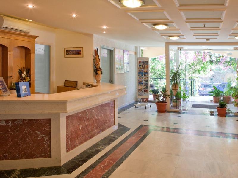 Empfangsbereich mit Marmor-Theke, heller Bodenfliese und großen Fenstern, Pflanzen sichtbar.