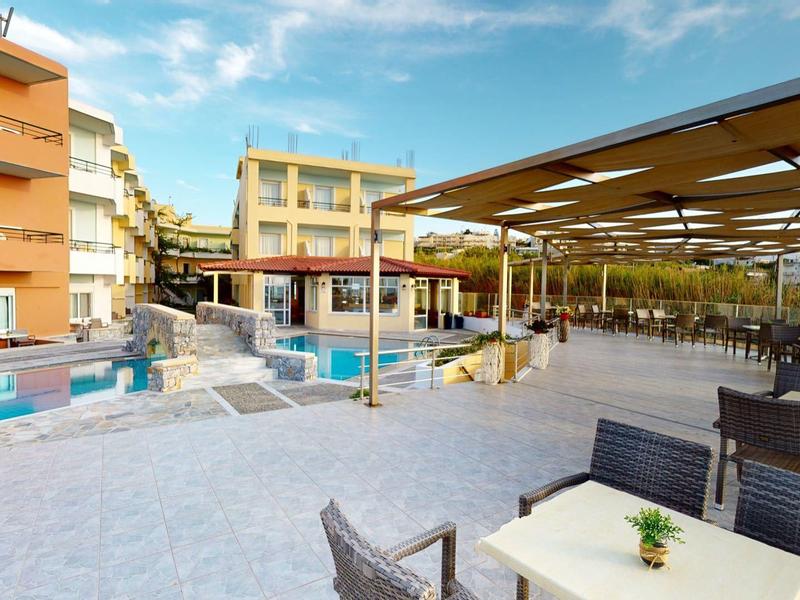 Große Terrasse mit Tischen, Stühlen, Pool und orangefarbenem Hotelgebäude unter blauem Himmel.