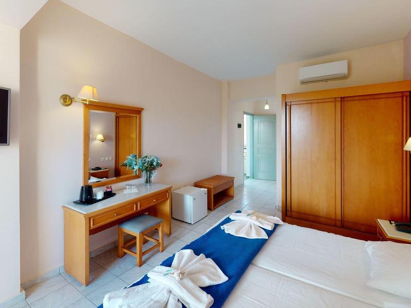 Gemütliches Hotelzimmer mit Doppelbett, Holzmöbeln, Schrank, Spiegel, Fernseher und Klimaanlage.