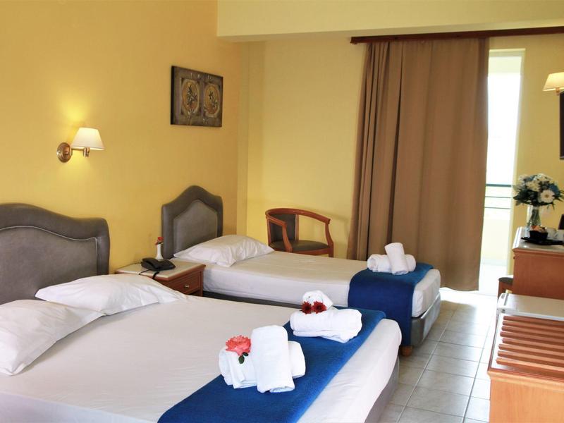 Hell eingerichtetes Hotelzimmer mit zwei Betten, weißen Handtüchern und dunklen Vorhängen.