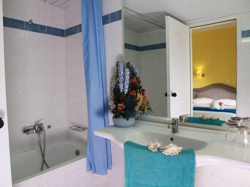 Badezimmer mit heller Badewanne, blauem Duschvorhang, großem Spiegel und Türkis-Handtuch.