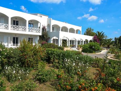 Edificio dell'hotel bianco con balconi accanto a un rigoglioso giardino sotto un cielo blu.