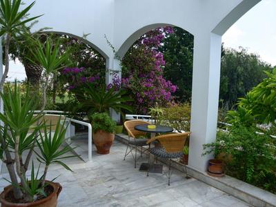 Terasa s bílými oblouky, rostlinami a zahradním stolem se židlemi v zeleném prostředí.