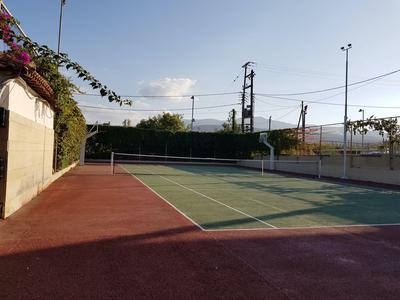 Campo da tennis all'aperto con superficie rossa e verde sotto un cielo limpido.