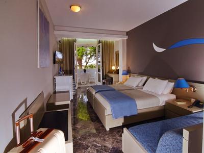 Moderní hotelový pokoj s velkou postelí, psacím stolem a výhledem na terasu se stromy.