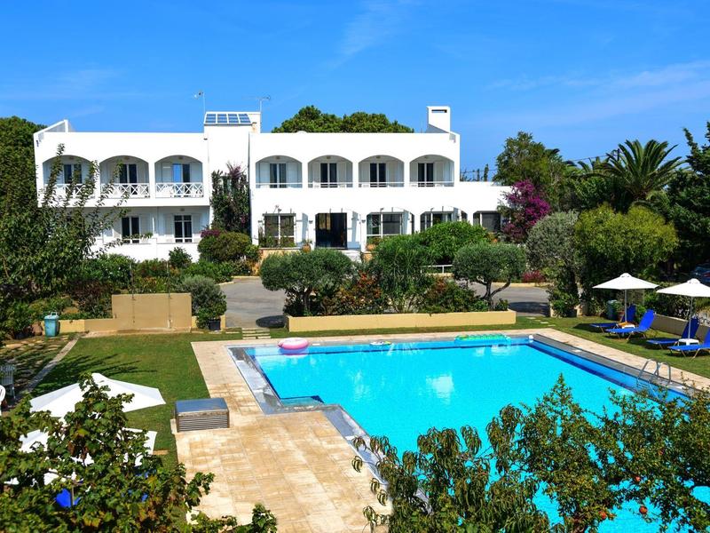 Bílý hotel s bazénem a slunečnou zahradou pod modrou oblohou.