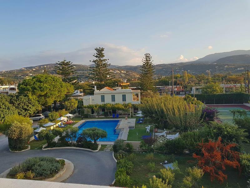 Pohled na hotel s bazénem, zahradou a okolními horami za jasné oblohy.