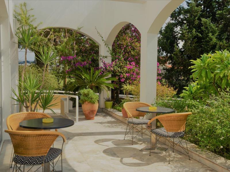 Vstup do hotelu s obloukem, stolem a židlemi v přírodním prostředí s rostlinami