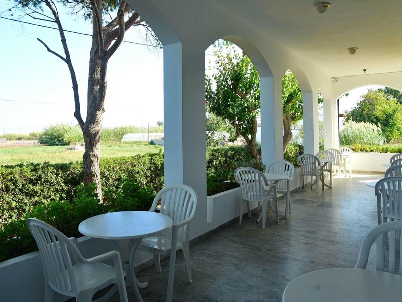 Zastřešená terasa s bílými židlemi a stoly obklopená zelenou krajinou.