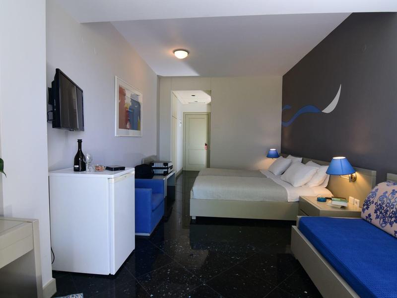 Moderně zařízený hotelový pokoj s manželskou postelí, pohovkou a televizí s plochou obrazovkou.