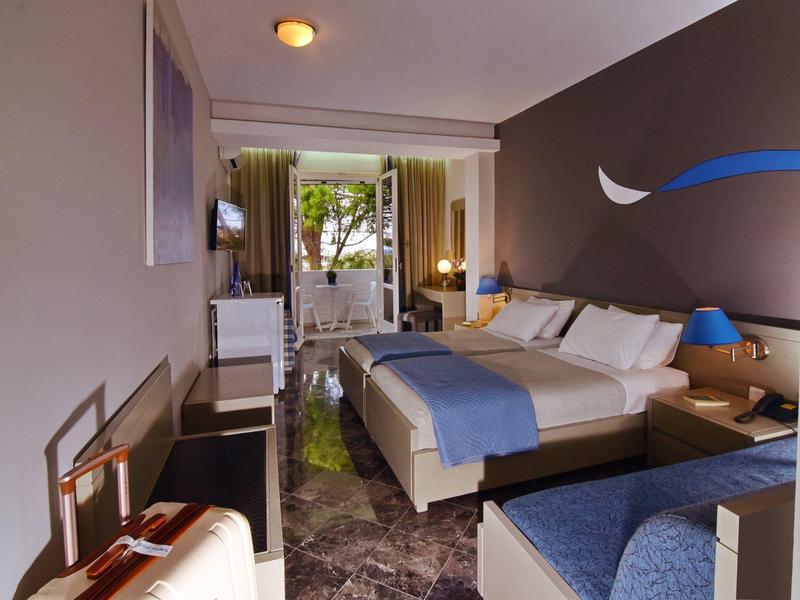 Moderní hotelový pokoj s velkou postelí, psacím stolem a výhledem na terasu se stromy.