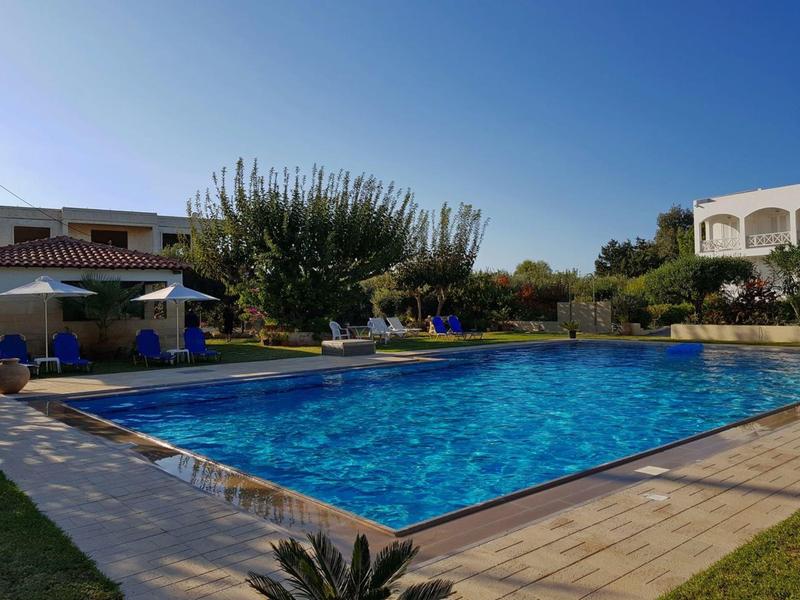 Velký čistý bazén obklopený lehátky a stromy pod modrou oblohou.